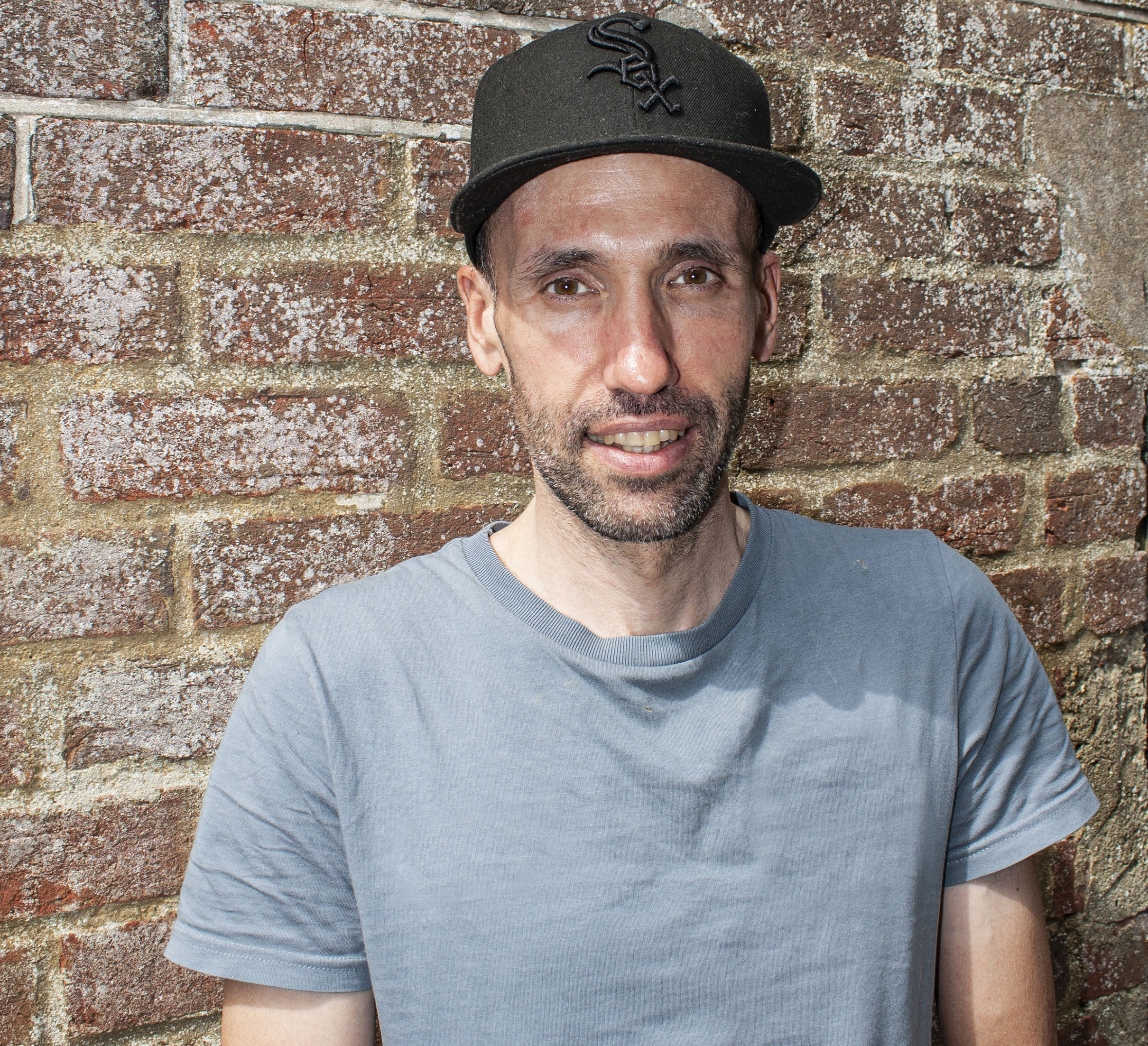 Aaron Borrill wearing a cap against a brick wall