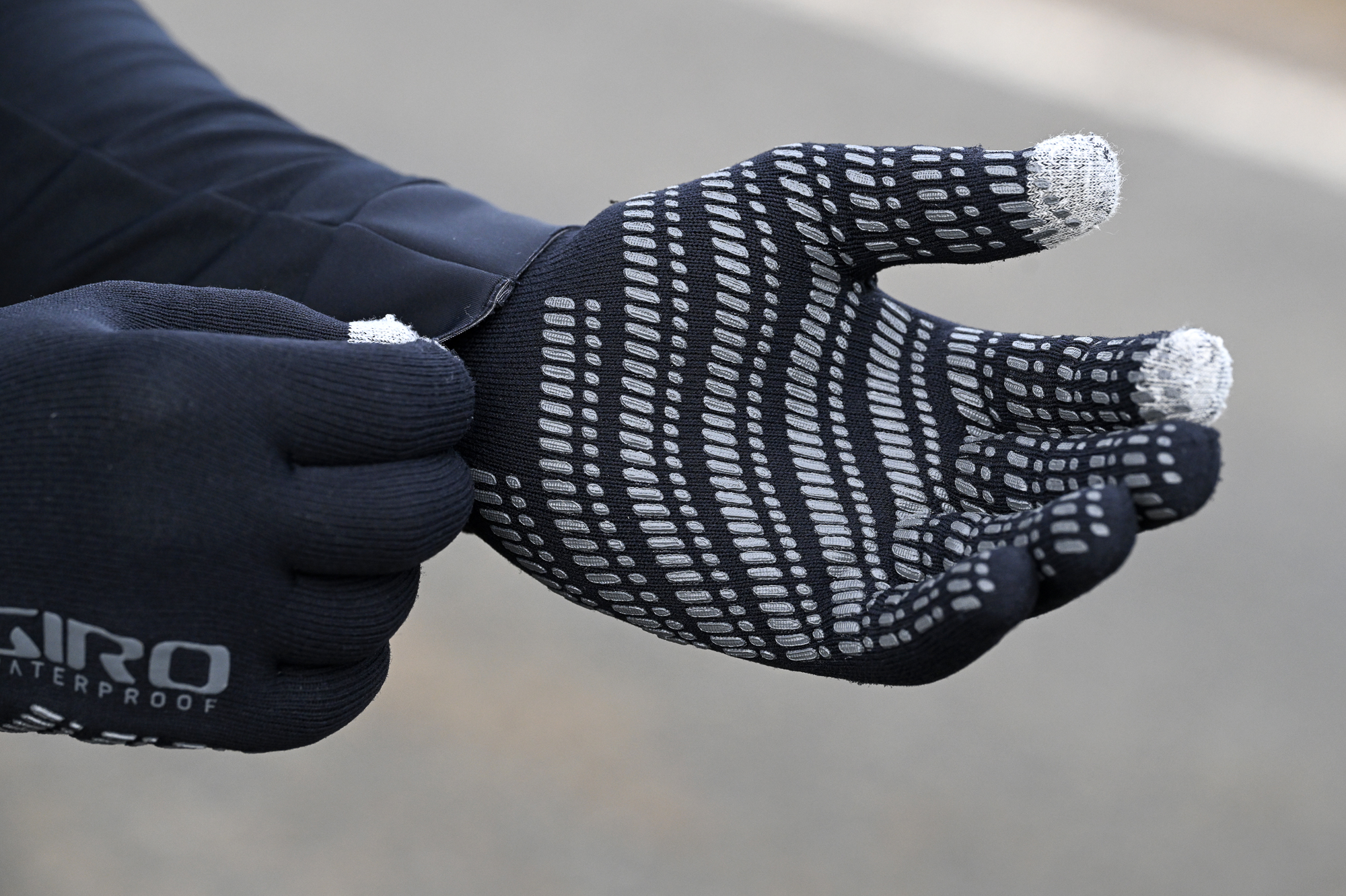 close up of a man adjust the cuff of his jacket whilst wearing black gloves with the word 'Giro' on them