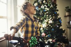 Boy, child and surprised with christmas bike in relax family home and house living room in festive holiday, gift opening and celebration. Kid, wow face and shocked and xmas bicycle present in lounge