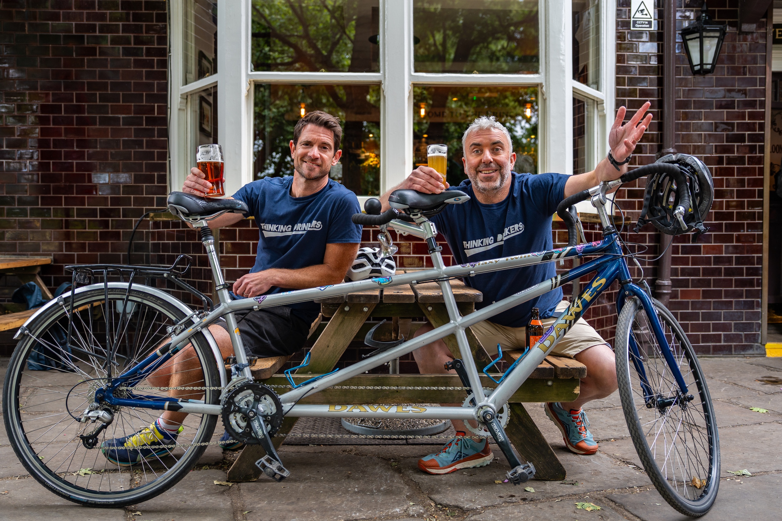 Ben and Tom with their tandem, raising a glass outside a pub